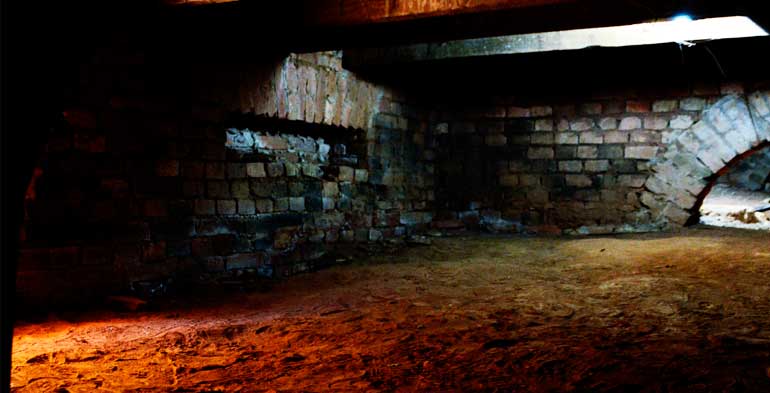 Imagem dramática de uma senzala doméstica com o chão em terra batida e paredes de tijolo