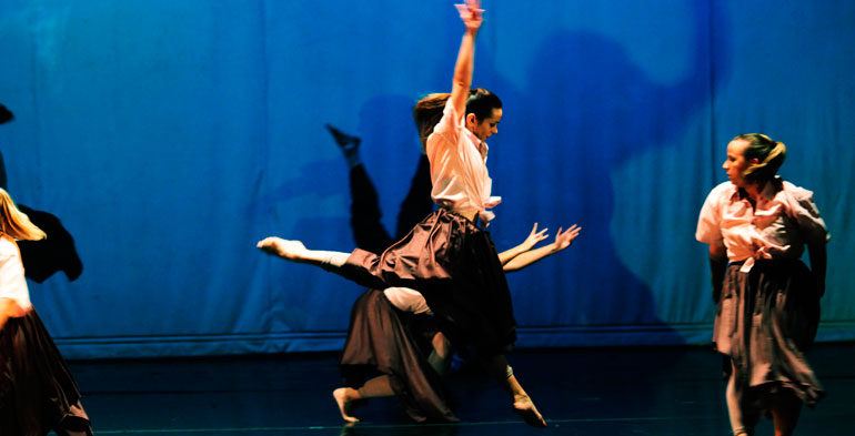 Performance do grupo Emy32 com destaque no centro do palco com um salto